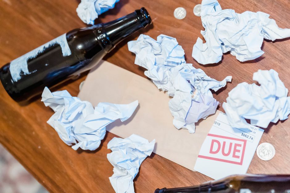 A chaotic scene with overdue bill, beer bottles, and crumpled papers on a wooden table.